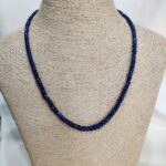 Handcrafted sapphire necklace with faceted blue beads displayed on a neutral woven bust, highlighting Afghan gemstone artistry and emotional symbolism.