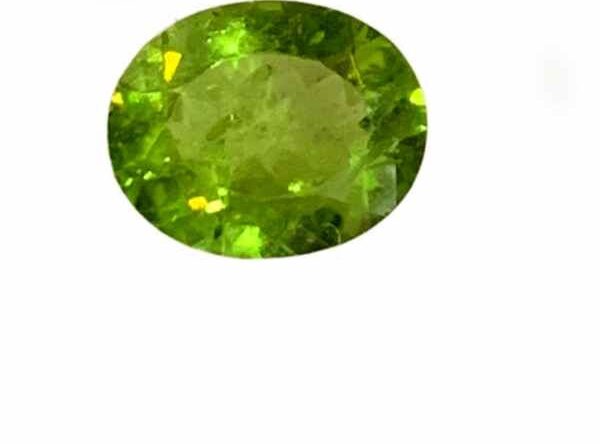 A vivid green Peridot gemstone with an oval cut, placed against a clean white background. The stone features sharp, symmetrical facets that reflect light delicately, highlighting its clarity and natural brilliance. The overall hue is a soft to medium olive green, evoking freshness and calm.
