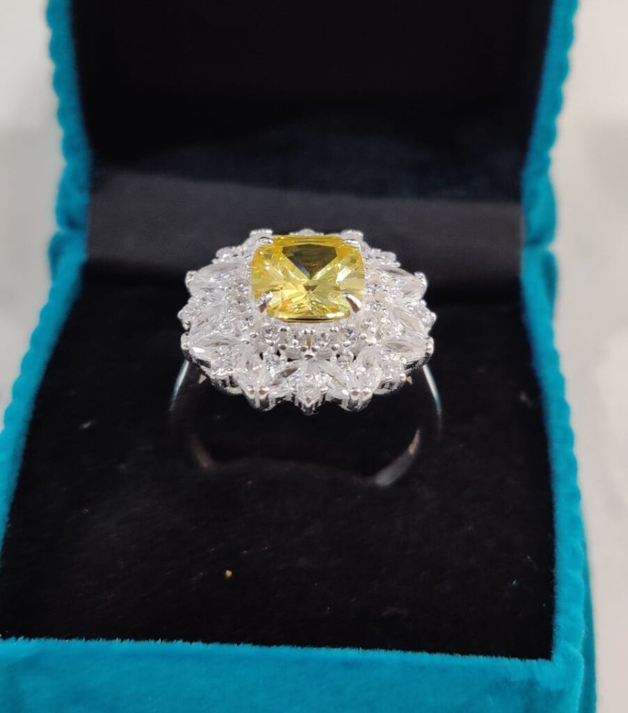 "Zircon special engagement ring in rhodium silver featuring a golden-yellow zircon centerpiece surrounded by diamond-like stones, displayed in a turquoise velvet box."