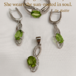 A graceful peridot jewelry set—comprising a silver ring, pendant, and earrings—artfully displayed with soft lighting that highlights the olive-green brilliance of each gemstone. The background is clean and muted, allowing the stones to radiate serenity. Overlaid in elegant font is a poetic quote by Dr. Bakht: “She wears growth, not glitter. She wears light, not luxury. She wears the sun—rooted in soul.” The composition evokes renewal, emotional elegance, and nature’s quiet resilience.