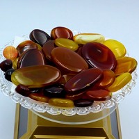 Polished agate and carnelian stones in rich amber, honey, and deep red hues displayed in a crystal dish—used in spiritual jewelry and healing rituals.
